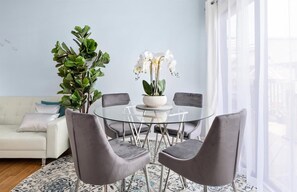 Ein modernes Wohnzimmer mit einem Glastisch, grau gepolsterten Stühlen, einem weißen Sofa und einer großen Grünpflanze.