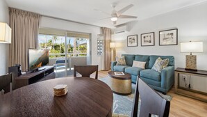 A modern living room with a round dining table, a blue sofa, and a ceiling fan. - Plantation Hale Suites H15, Top Floor, AC, Walk to Beach (Kapaa)