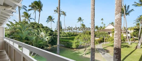 A balcony with a view of a well-maintained garden, including palm trees and neatly trimmed hedges.