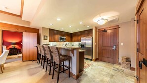 Una cocina moderna con armarios de madera, un refrigerador de acero inoxidable y una zona de bar con taburetes altos.