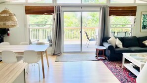 A spacious living area with a large sliding glass door leading to a balcony, a dining table with chairs, a sofa, and a coffee table.
