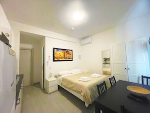 A hotel room with a bed, bedside table, and a dining table with chairs.