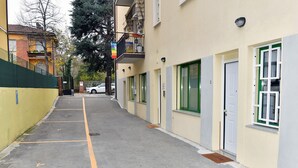 Una calle estrecha con una hilera de edificios de una sola planta, cada uno con una puerta y una ventana. Un coche está estacionado en la calle, y se ve una bandera en uno de los edificios.
