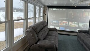 Une pièce dotée d’une grande fenêtre, d’un canapé gris et d’un écran de projection affichant l’interface d’un service de diffusion en continu.
