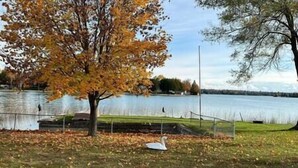 Un parc avec un lac, un arbre aux feuilles d’automne et un banc.
