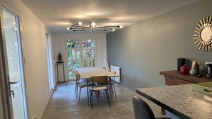 Un comedor con mesa y sillas, una encimera de cocina con electrodomésticos, y un ventanal con vistas a zonas verdes.
