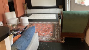 Una sala de estar con un sofá, una mesa de centro, un tapete estampado, un televisor y una ventana con una planta.