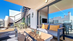 A modern living room with a sofa, coffee table, and dining area. A staircase leads to an upper level. - Penthouse Apartment with Sea and Pool Views (San Javier)
