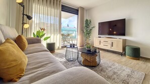 A modern living room with a sofa, a coffee table, a TV, and a balcony with a view. - Penthouse Apartment with Sea and Pool Views (San Javier)