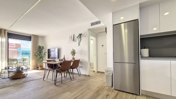 A modern kitchen with a stainless steel refrigerator, a dining area with a table and chairs, and a view through a large sliding glass door. - Penthouse Apartment with Sea and Pool Views (San Javier)