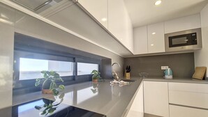 A modern kitchen with a black induction cooktop, white cabinets, and a microwave. - Penthouse Apartment with Sea and Pool Views (San Javier)