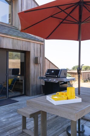 An outdoor patio with a wooden table, a barbecue grill, and a red umbrella.