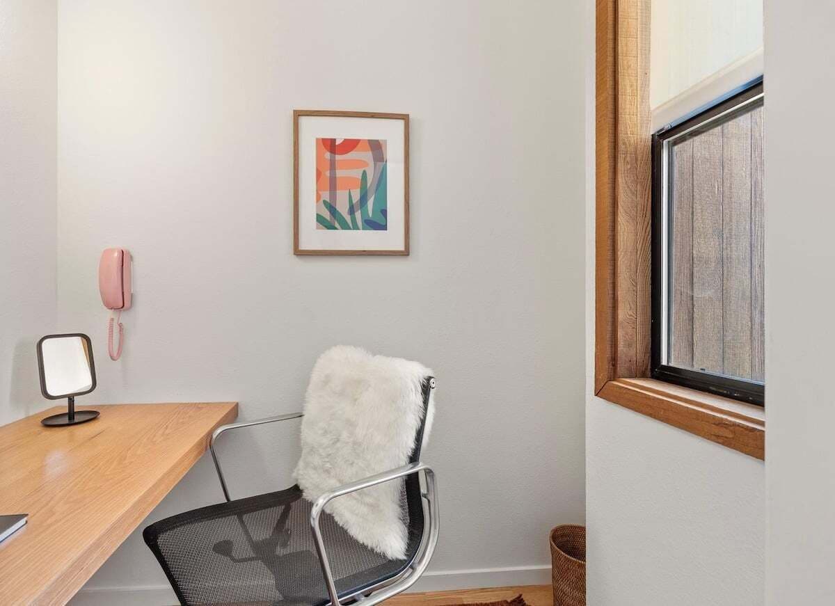 A room with a desk, chair, framed artwork, a telephone, and a window.