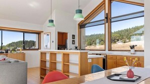 A modern kitchen with wooden cabinets, a dining area with a marble countertop, and large windows offering a view of the outdoors.