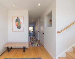 A hallway with a bench, a colorful rug, and a staircase with a wooden handrail. - Hawk Haven | Ocean Views, Hot Tub & Cozy Fireplace (Sea Ranch)