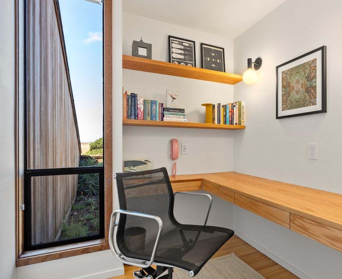 A modern office space with a desk, chair, bookshelves, and a window with curtains.
