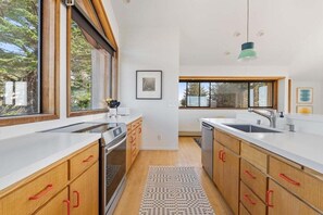 A modern kitchen with wooden cabinets, stainless steel appliances, and large windows. - Hawk Haven | Ocean Views, Hot Tub & Cozy Fireplace (Sea Ranch)