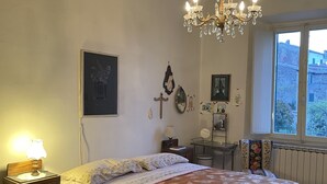 Une chambre à coucher avec un grand lit, un lustre, une commode, une table de chevet, une fenêtre donnant sur un beau paysage et un radiateur.