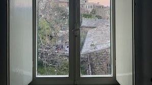 Une pièce dotée d’une grande fenêtre donnant sur une ville historique, avec ses bâtiments en pierre et un arbre au premier plan.