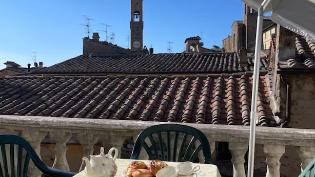 Une terrasse avec une table dressée pour le thé, agrémentée d’une théière, de tasses et de pâtisseries. On aperçoit un clocher en arrière-plan.