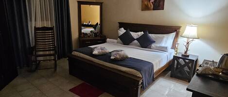 A hotel room with a bed, a nightstand, a lamp, a chair, a mirror, and a painting on the wall.
