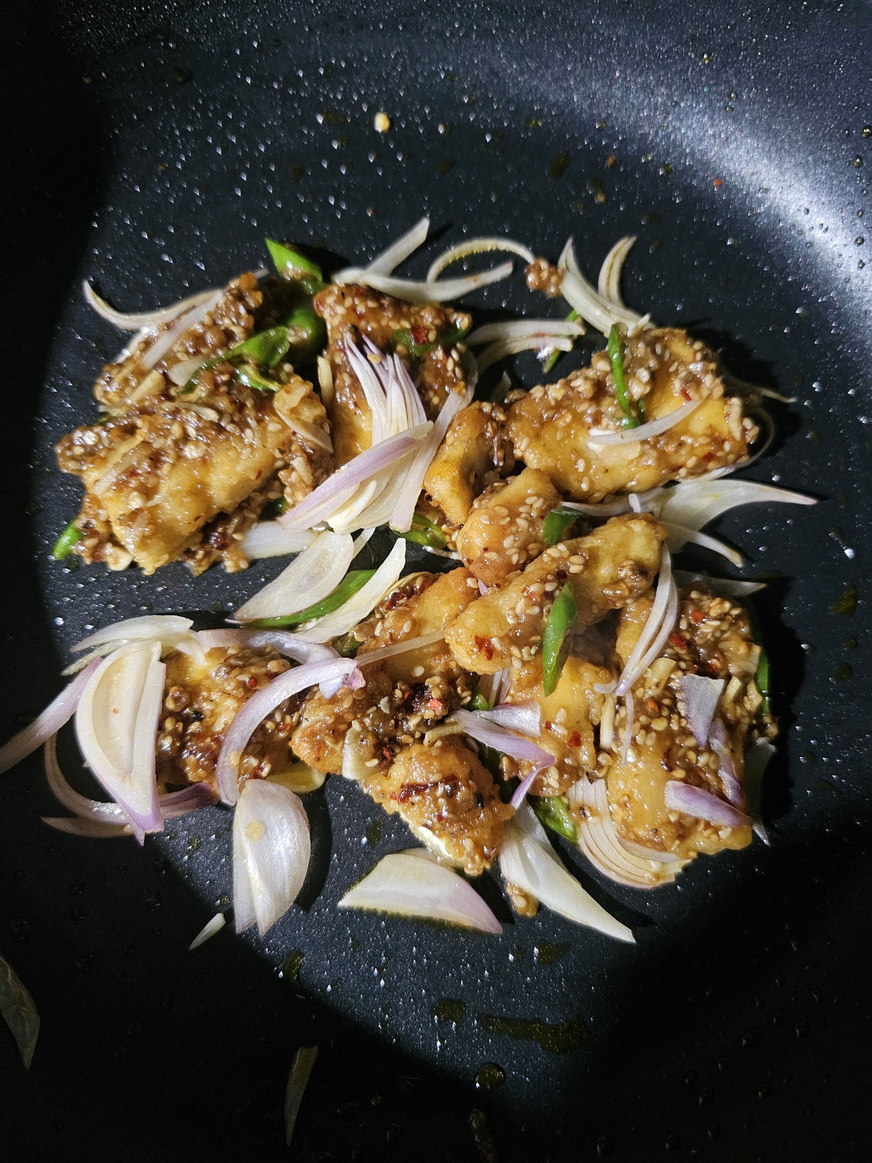 Primer plano de un plato con trozos de pollo, pimientos verdes y cebolla en rodajas en una sartén.