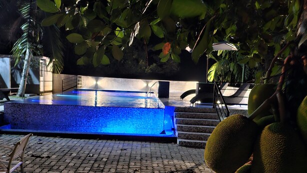 A pool area with a blue-lit water feature, a staircase, and a chair. - Ellakanda Nature Villa  (Welipenna)