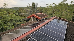 A solar panel installation on a building with a red roof, surrounded by lush greenery and hills in the background. - Ellakanda Nature Villa  (Welipenna)
