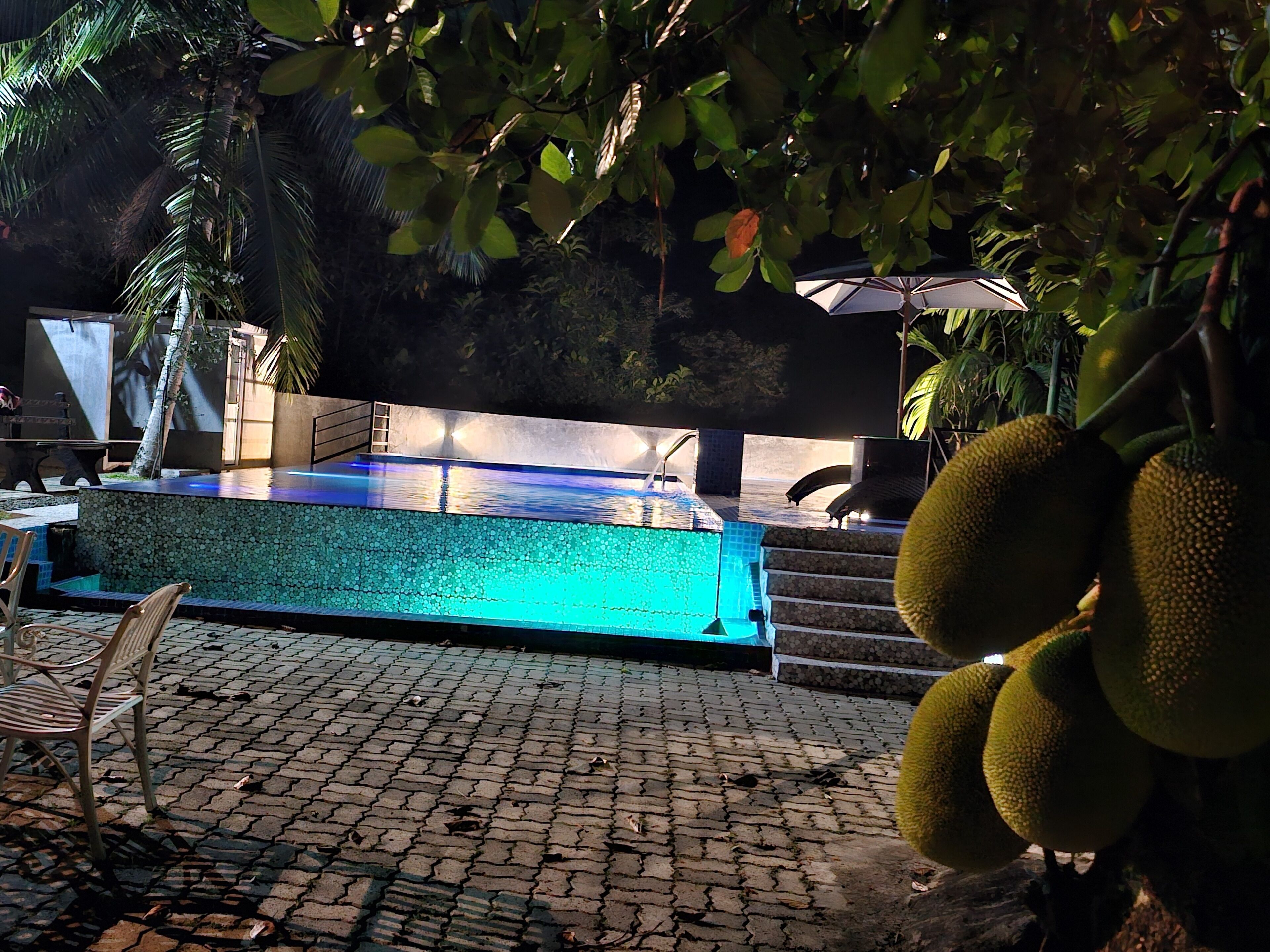 Una piscina con borde de azulejos, rodeada de una zona pavimentada con sillas y una escalera que conduce a un área de descanso cubierta.