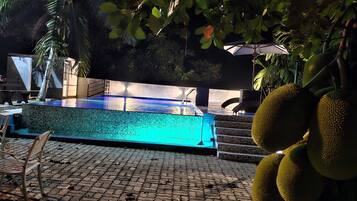 Una piscina con borde de azulejos, rodeada de una zona pavimentada con sillas y una escalera que conduce a un área de descanso cubierta.