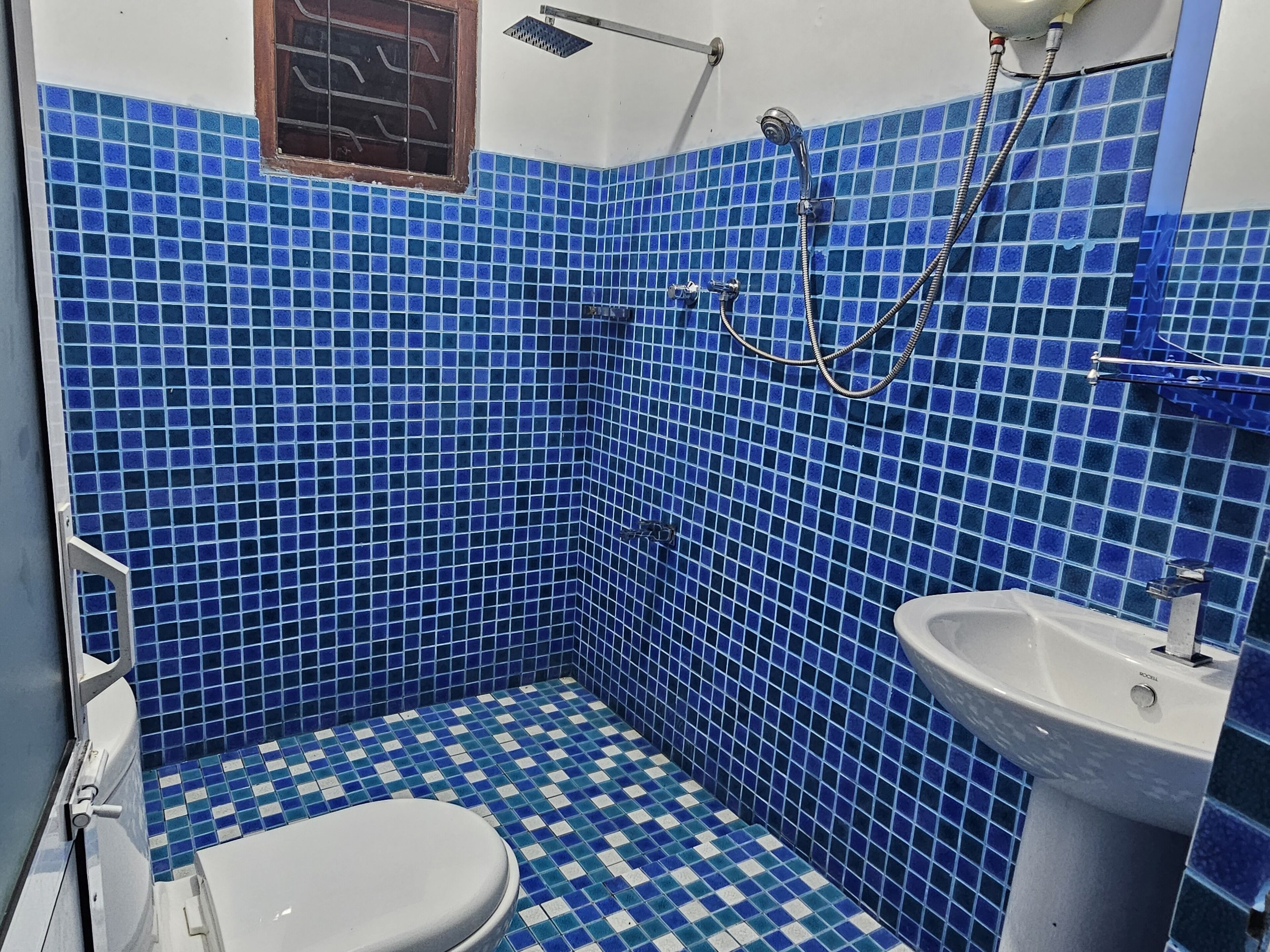 A bathroom with blue mosaic tiles, a white toilet, and a sink.