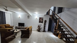 A spacious living room with a sofa, a coffee table, and a TV. There is a staircase with a railing leading to an upper floor. - Ellakanda Nature Villa  (Welipenna)
