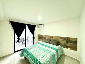 Um quarto com cama, janela com cortinas, uma cadeira e uma mesa na varanda.