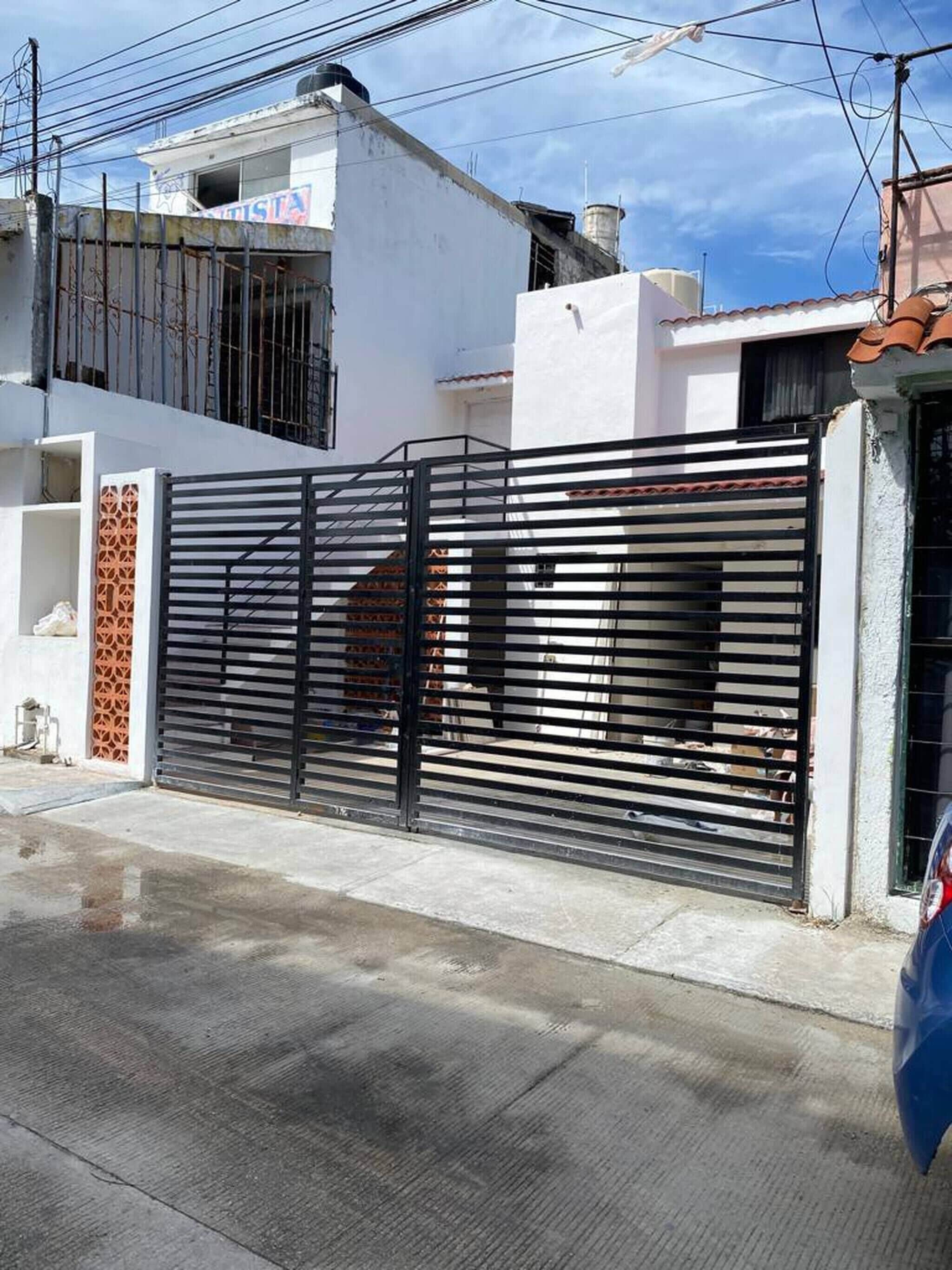 Zona residencial cerrada con un edificio blanco, una reja negra y un coche azul estacionado cerca.