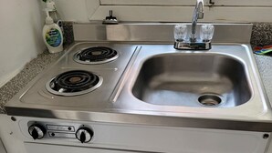 A compact kitchen with a stove, sink, and storage cabinets. - The Cottages at Gull & Castle Cabin #1 (Wasagaming)