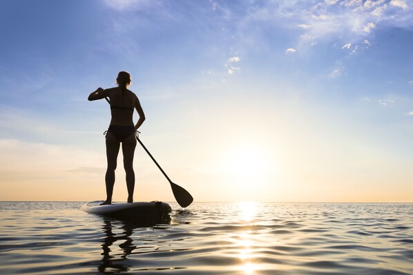 En person padler på paddleboard i rolige vand under solnedgang.