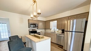 A modern kitchen with stainless steel appliances, a wooden island, and a bar stool.