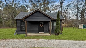 A small, dark-colored wooden house with a front porch and a door.