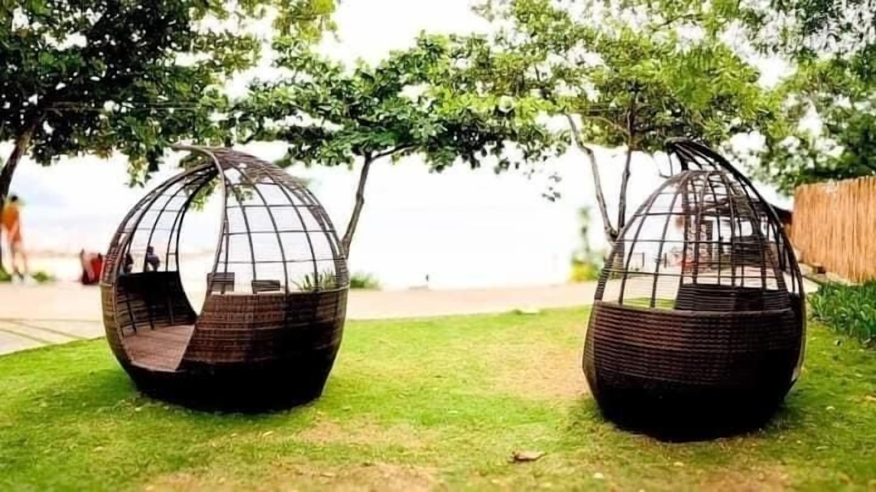 Two spherical outdoor seating areas with a wicker frame and a bench inside.