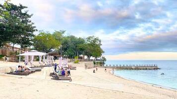 A beach with sun loungers, umbrellas, and a pier extending into the water.