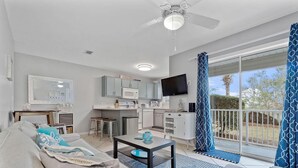 A modern living room with a sofa, coffee table, and a kitchen area with a microwave and TV.