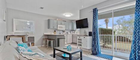 A modern living room with a sofa, coffee table, and a kitchen area with a microwave and TV.