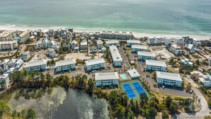 An aerial view of a coastal resort with multiple buildings, a beach, and a tennis court.