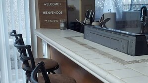 A kitchen area with a bar counter, stools, a welcome sign, and a clock on the wall. - Cozy Retreat in Rosarito Near Beaches and Dining (Playas de Rosarito)