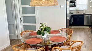 A dining area with a round glass table, wicker chairs, and a central hanging light fixture. - FLASH SALE - just steps to beach. 2BR/1BA.Dogs welcome! Perfect ratings. (Englewood)