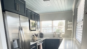 A modern kitchen with dark cabinets, stainless steel appliances, and a large window providing natural light. - FLASH SALE - just steps to beach. 2BR/1BA.Dogs welcome! Perfect ratings. (Englewood)