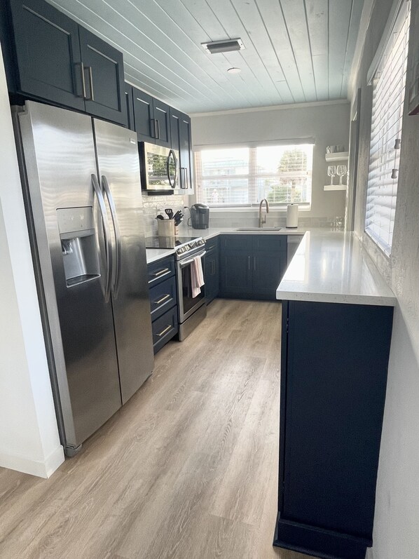 A modern kitchen with dark cabinets, stainless steel appliances, and a large window providing natural light.