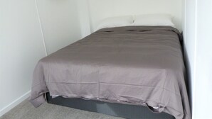 A single bed with a grey bedspread in a room with white walls and a white headboard. - Retraite Saint Boniface/St. Boniface Retreat (Winnipeg)
