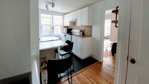 A kitchen with white cabinets, a black chair, and a window. - Retraite Saint Boniface/St. Boniface Retreat (Winnipeg)