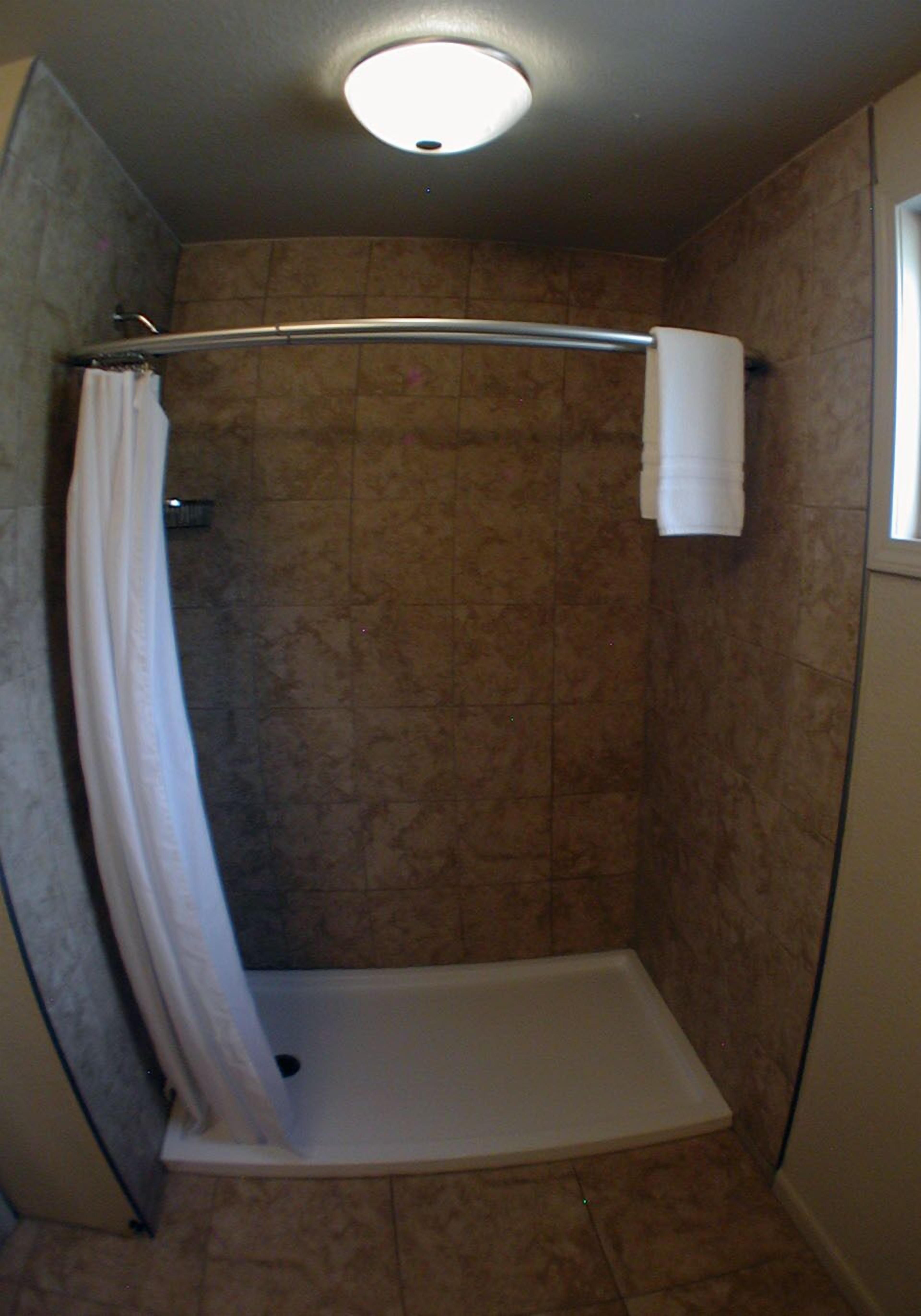 A small, enclosed shower area with a shower curtain, a towel hanging on the wall, and a ceiling light.
